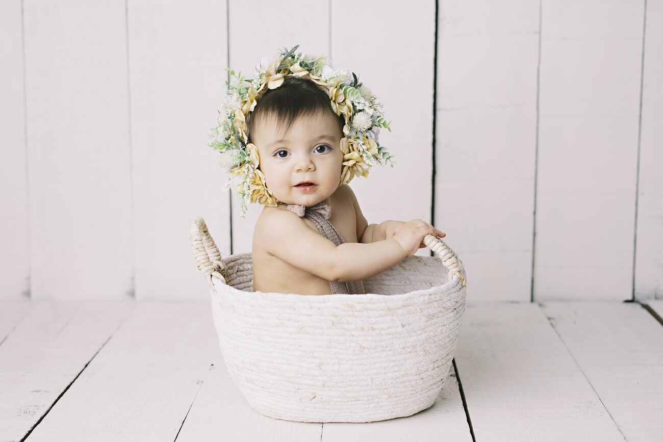 Baby in floral bonnet sitting in woven basket, timeless Boise baby photography