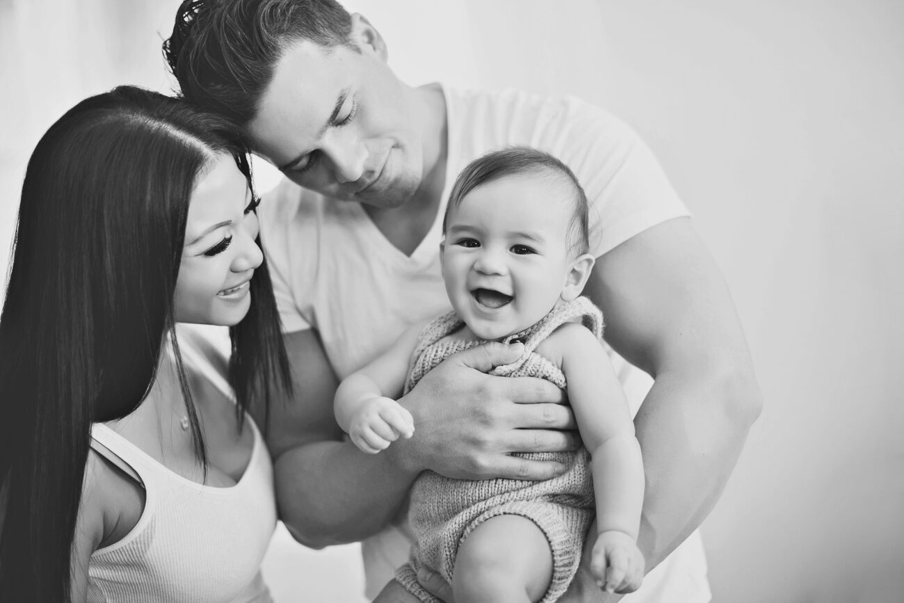 Black and white photo of laughing baby held by parents, Boise baby photography