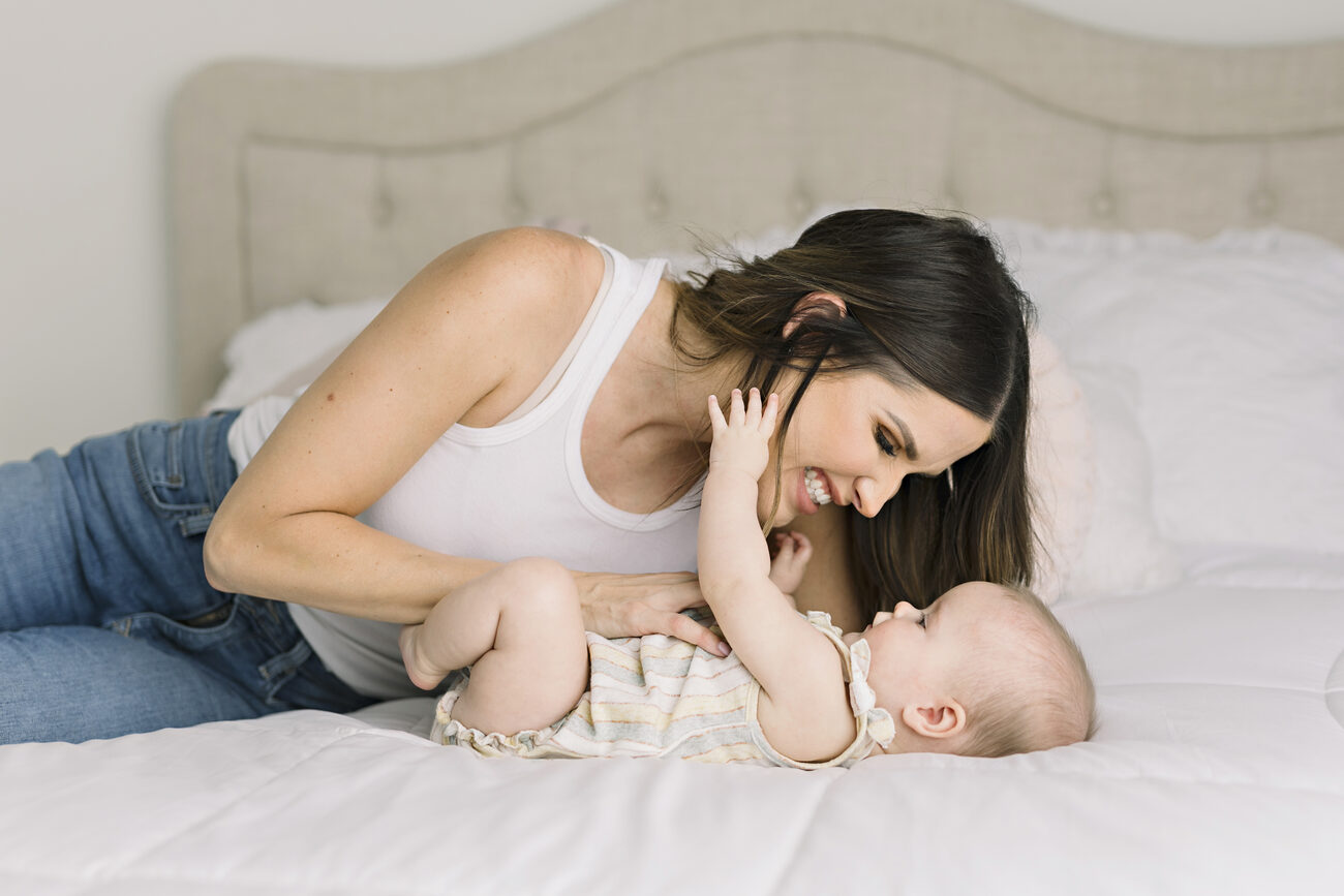 Mother laughing and playing with baby on the bed, in-home Boise baby photography session